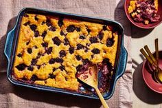 blueberry cobbler in a baking dish with two plates and spoons next to it