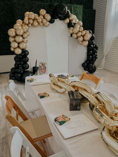 the table is set up for a party with black, gold and white balloons in the background