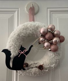 a wreath with ornaments and a black cat hanging from it's side on a door