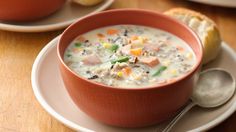 a bowl of soup on a plate next to a piece of bread with a spoon