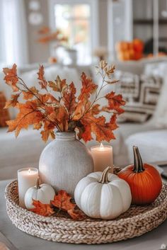 a table topped with white pumpkins and candles next to a vase filled with leaves