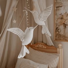 two white birds are hanging from a string in a room with curtains and bedding