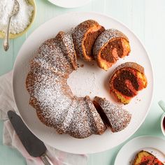 a bundt cake with powdered sugar on top sits on a plate next to other desserts