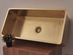 a gold sink on top of a wooden cabinet with a potted plant in it