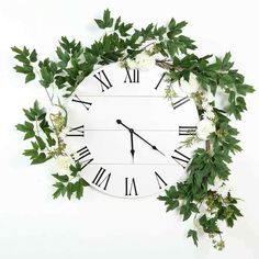 a white clock with green leaves and flowers around it