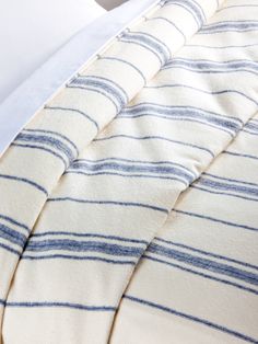 a bed with blue and white striped comforter on it's side, next to an unmade pillow