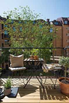 two chairs and a table on a balcony with potted plants in the foreground