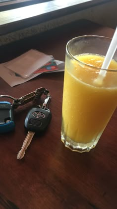 a glass of orange juice next to two car keys and a drink on a table