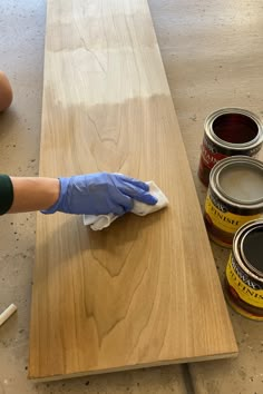 a person in blue gloves is wiping down some paint on a wooden table with two cans