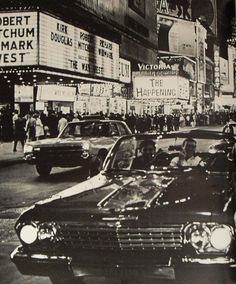 an old black and white photo of people in a car on a street with marquee signs