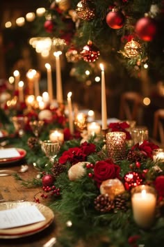 a long table with candles and christmas decorations on it, surrounded by greenery and red roses