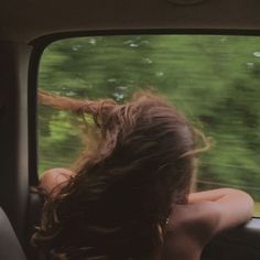 a woman sitting in the back seat of a car with her hair blowing in the wind