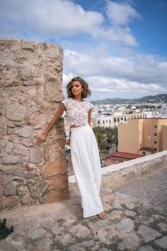 a woman leaning against a stone wall with her hands on the side and looking off into the distance