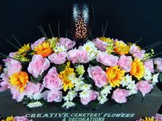 pink and yellow flowers are in a vase on a table with a sign that says creative cemetery flowers & decorations