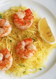 some shrimp and noodles are on a white plate with lemon wedges next to it