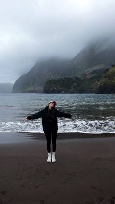 a woman standing on top of a beach next to the ocean with her arms outstretched