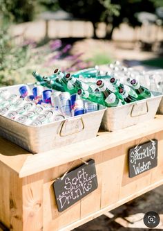 a wooden table topped with lots of bottles of beer next to a sign that says soft drinks