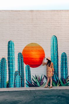 a woman is standing in front of a wall painted with cactus and oranges on it