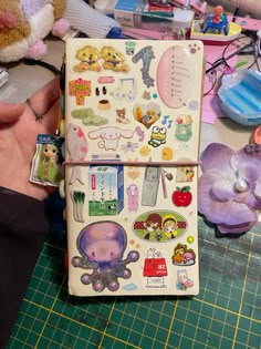 a person holding a small notebook covered in stickers and magnets next to a stuffed animal