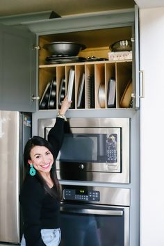 a woman is standing in front of an oven with dishes on the shelves above her