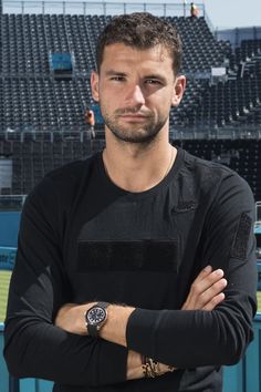 a man with his arms crossed standing in front of a tennis court and looking at the camera