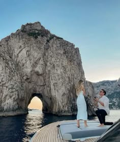 a man and woman standing on the bow of a boat in front of a rock formation