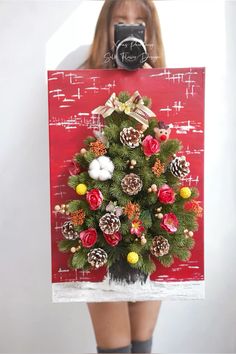 a woman holding up a christmas card with pine cones and other decorations on the front