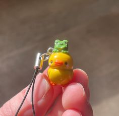 a tiny yellow rubber ducky with a frog on its head sitting on a key chain