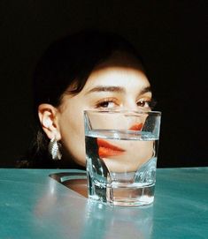 a woman sitting at a table with a glass of water in front of her face