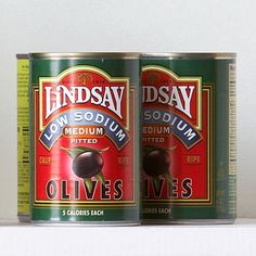 two cans of olives sitting on top of a white shelf next to each other