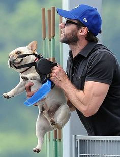 a man holding a dog in his arms while wearing a blue hat and black shirt