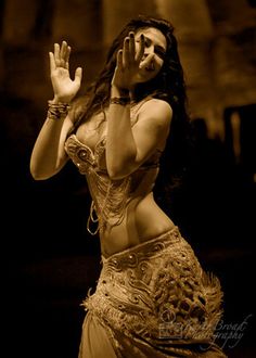 a woman in a belly dance outfit is holding her hands up to the side while she holds