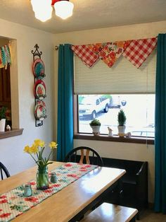 a dining room table with flowers in vases on it and blue curtains hanging from the window