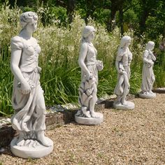 four statues of women are lined up on the ground in front of some grass and bushes