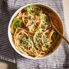 a bowl filled with pasta and broccoli on top of a blue towel next to a wooden spoon