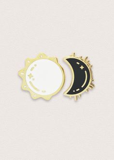 two enamel pins with the moon and sun on them, one black and one white