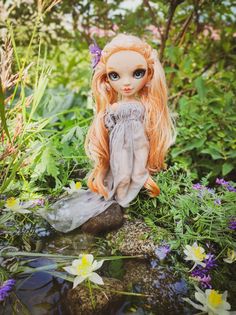 a doll sitting on top of a rock in the grass next to flowers and plants