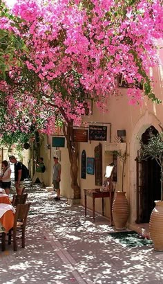 an alley with tables and chairs lined up against the side of it, covered in pink flowers