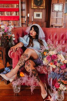 a woman sitting on top of a red couch with flowers in her hand and tattoos on her leg