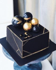 a black and gold square cake on top of a blue pedestal with three golden balls