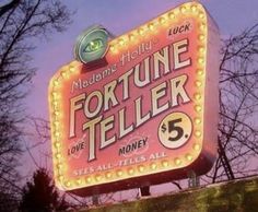 the fortune teller sign is lit up at night with pink sky behind it and trees in the foreground