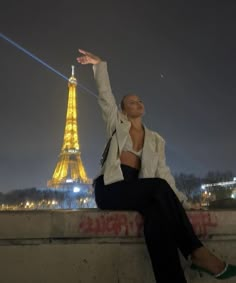 a woman sitting on top of a cement wall next to the eiffel tower