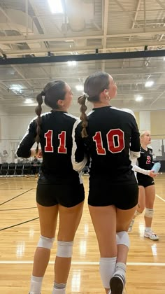 two girls in black uniforms standing on a basketball court with their arms around each other