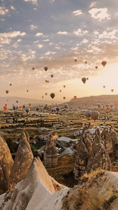 many hot air balloons are flying in the sky above some rocks and boulders at sunset