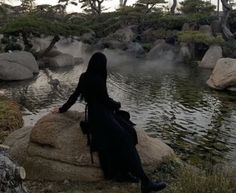 a woman sitting on top of a rock next to a body of water with steam rising from it