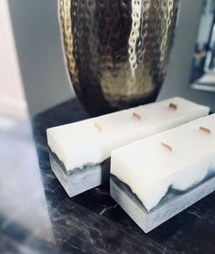 two pieces of white soap sitting on top of a counter next to a silver vase