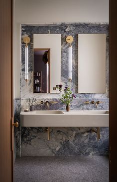 a bathroom sink with two mirrors above it and a vase filled with flowers on the counter