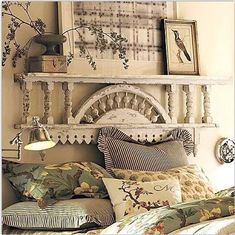 a bed with lots of pillows on top of it next to a lamp and pictures