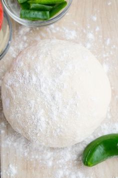 a ball of dough sitting on top of a wooden cutting board next to green peppers