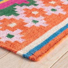 an orange, pink, and blue rug on a wooden floor with white wood floors